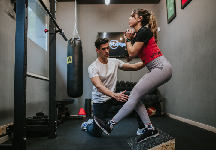 Imagem de uma aluna a fazer um exercício com auxílio de um profissional.